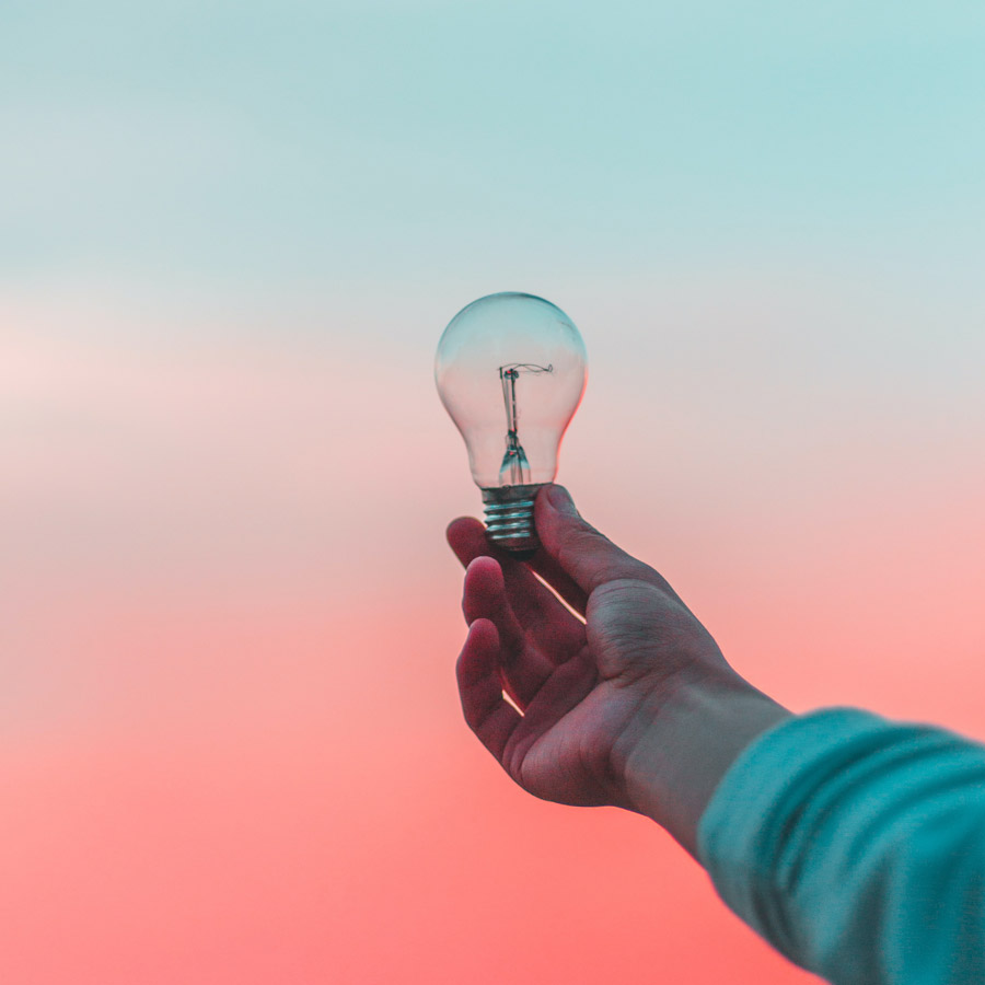 A hand holding a lightbulb with a sunset in the background. 