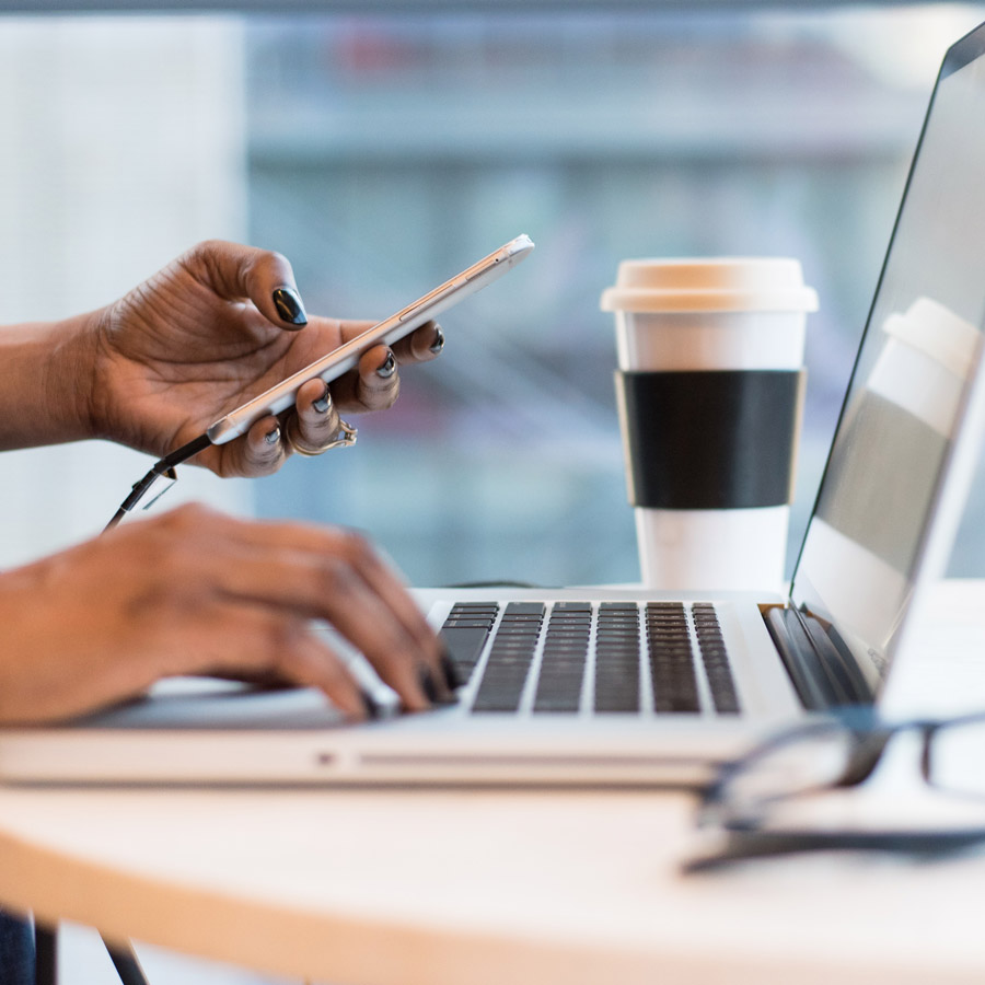 A hand holding a charging phone by a laptop.