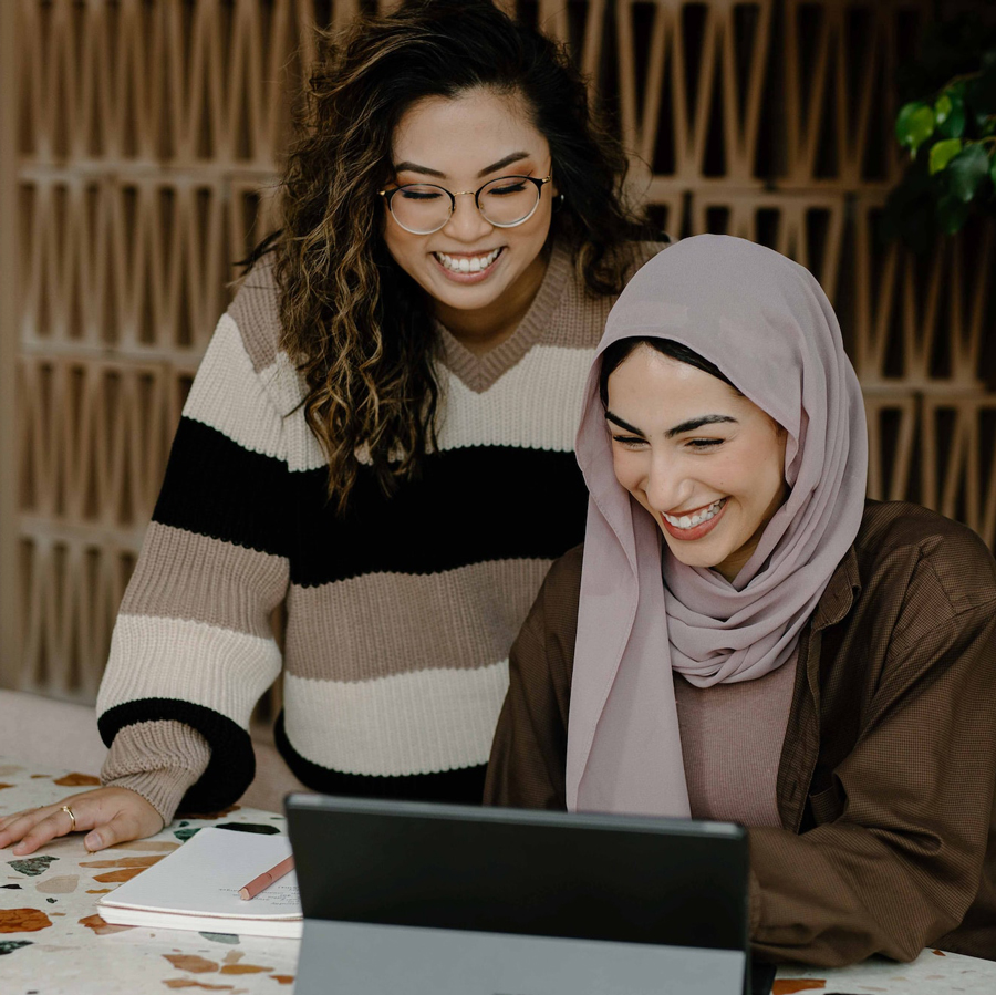 Two smiling women working at a desk with a laptop in an office.